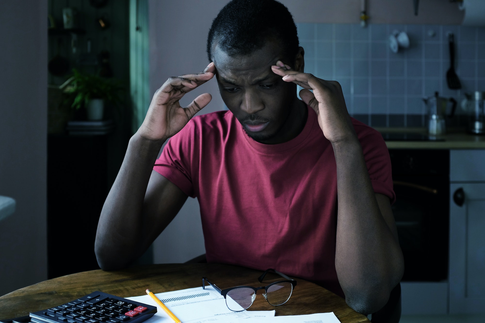 Young sad african american man tries to figure out details of bills looking at papers