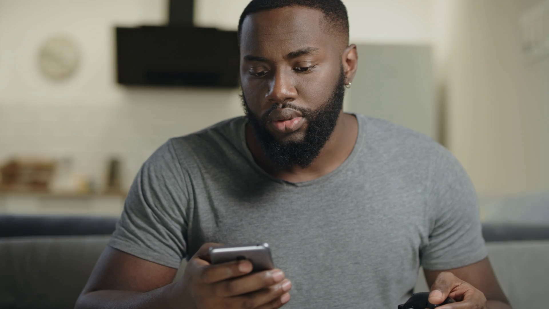videoblocks black man holding phone in hand at open kitchen concentrated guy texting in smartphone surprised male person looking at mobile phone at kitchen black male person getting news by cellphone bjxpt